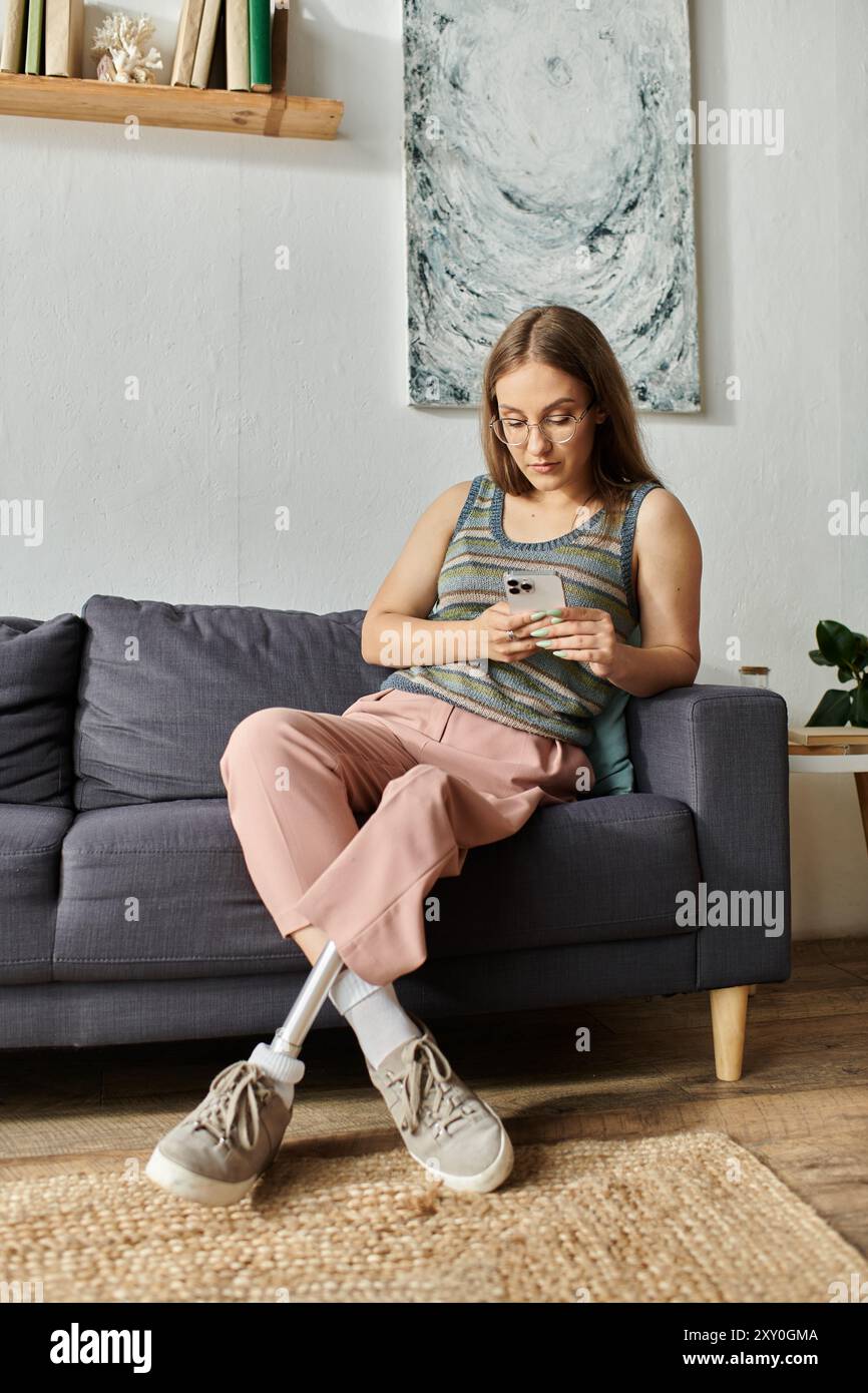 Une jeune femme avec une jambe prothétique se détend sur un canapé dans son salon moderne, engrossée dans son téléphone. Banque D'Images