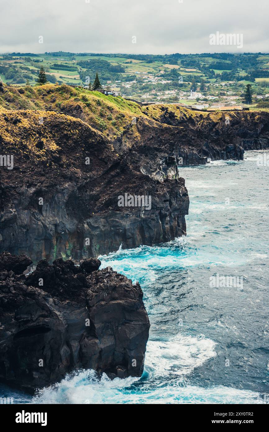 Une vue imprenable sur les Açores, mettant en valeur la côte accidentée avec des vagues s'écrasant contre d'énormes falaises sous un ciel couvert doux et luxuriant, collines verdoyantes Banque D'Images