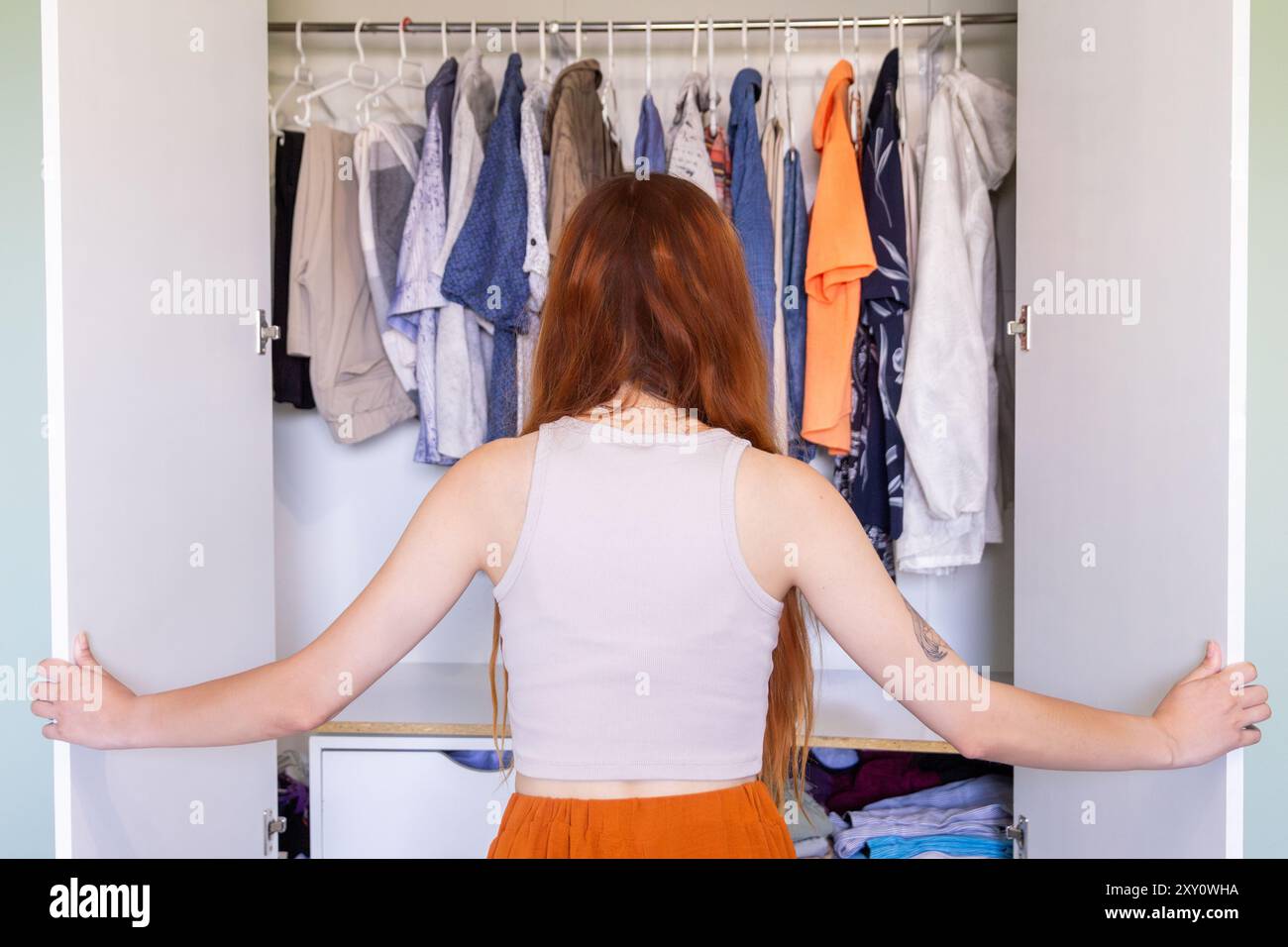 Vue arrière d'une femme méconnaissable rangeant et triant des vêtements dans son placard, considérant des articles à mettre en vente. Banque D'Images