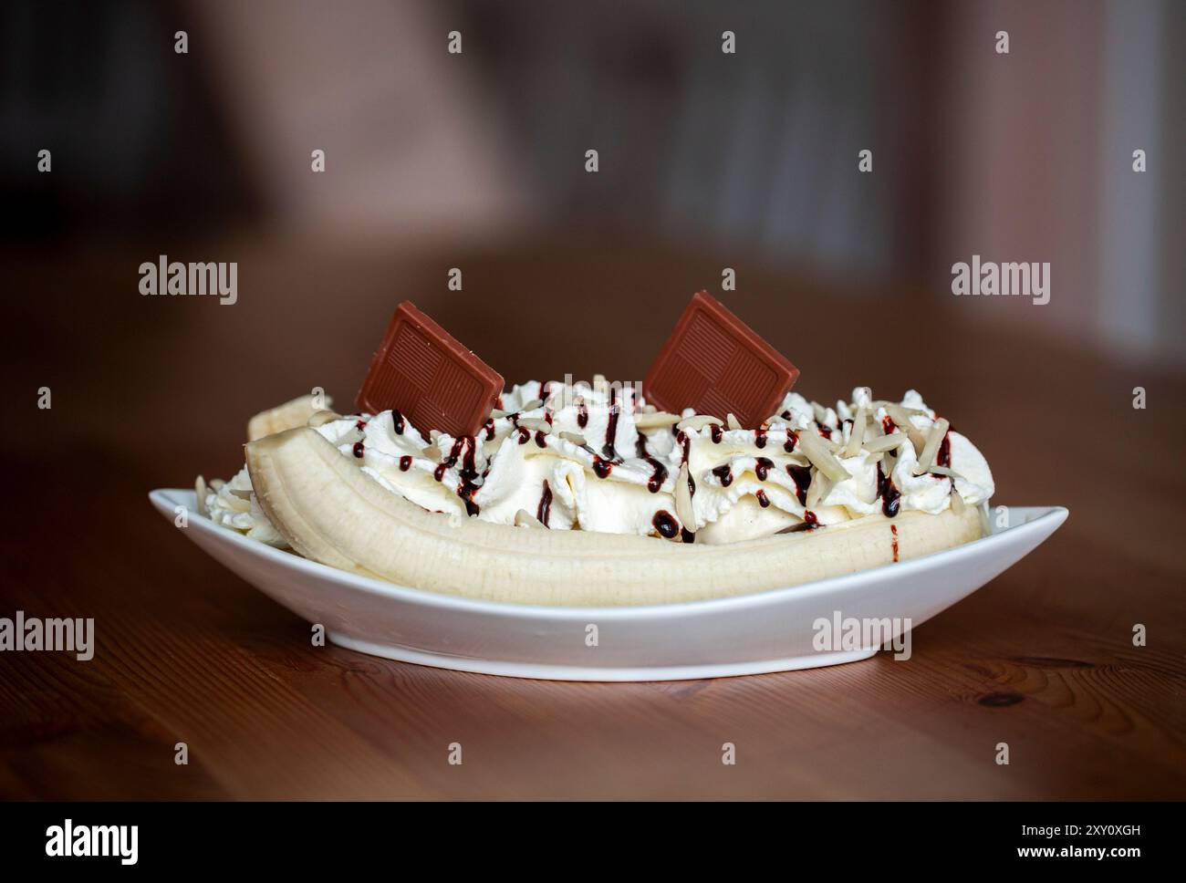 Une délicieuse fente de banane garnie de crème fouettée, de sirop de chocolat, de saupoudrées et de morceaux de chocolat, servie dans un bol blanc sur une table en bois. Banque D'Images