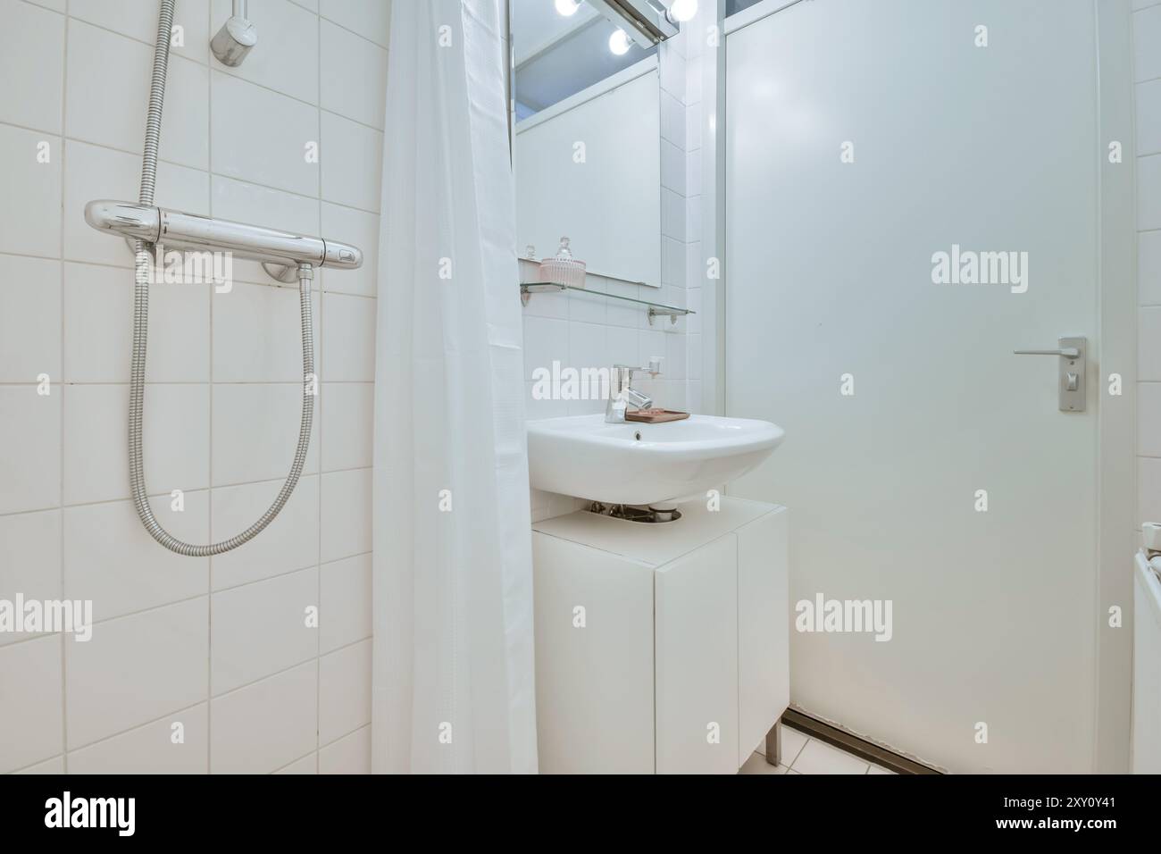 Salle de bains contemporaine avec lavabo sur pied blanc, douche avec rideau et murs carrelés clairs. Banque D'Images