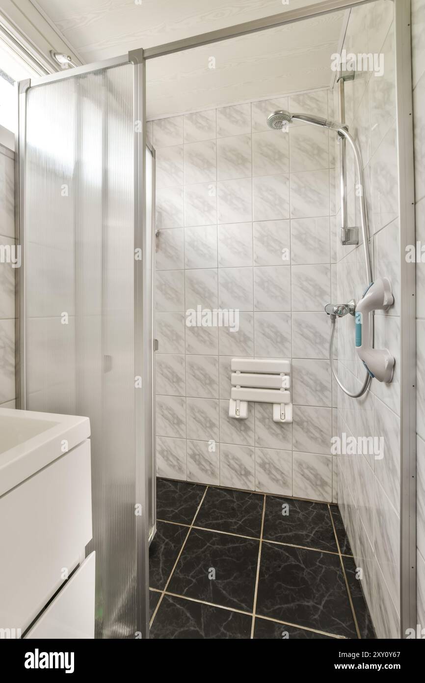 La salle de bains moderne et lumineuse est dotée d'une cabine de douche en verre, de carreaux muraux en marbre et de carreaux noirs élégants. Banque D'Images