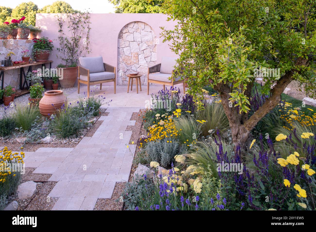 Un mur de calcaire derrière une terrasse pavée et un chemin entouré de plantes tolérantes à la sécheresse dans le jardin Meditrraneo. Designer : Katerina Kanatal Banque D'Images