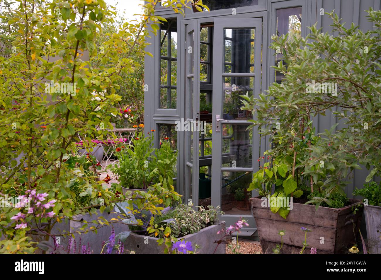 Les portes françaises du hangar de mise en pot s'ouvrent sur une terrasse de récipients remplis de plantes et de bordures herbacées dans le jardin sans tourbe. Concepteur : Arit Banque D'Images