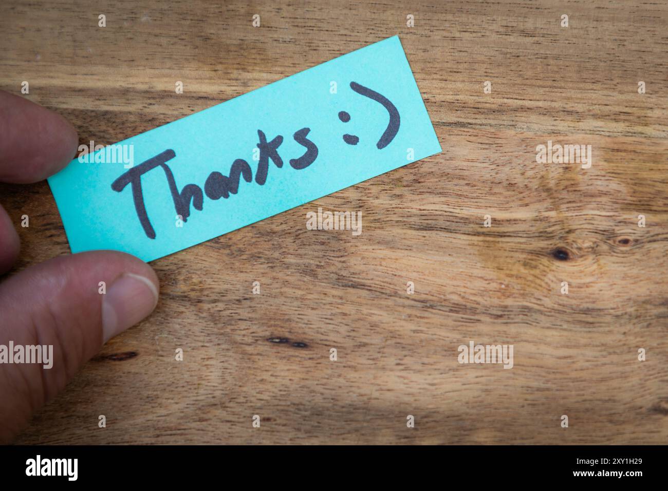Une main tenant un morceau de papier qui dit « Merci » dessus. Le papier est vert et a un visage souriant dessiné dessus. Concept de gratitude et d'appréciation Banque D'Images