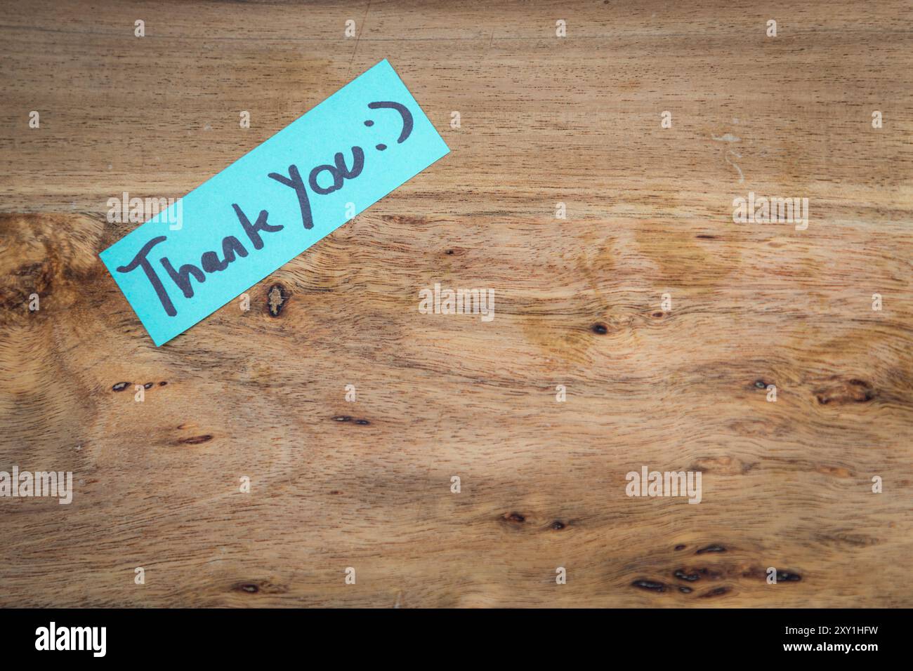 Une note de remerciement avec un visage souriant dessiné dessus. La note est sur une table en bois. Banque D'Images