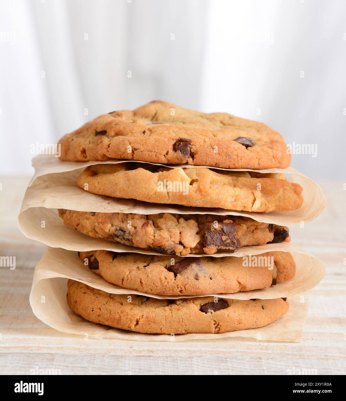 Gros plan d'une pile de biscuits frais cuits au four pépites de chocolat, farine d'avoine raisin, biscuits aux pépites de chocolat blanc sur papier parchemin. Format carré sur un w rustique Banque D'Images