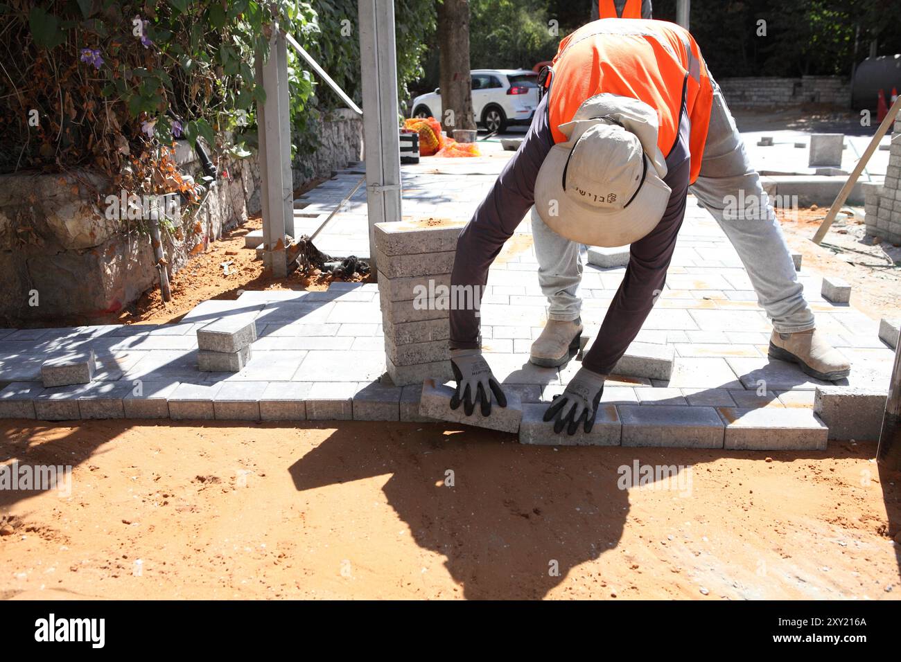 Travailleur palestinien avec gilet de protection met des briques sur des couches de béton comprimé et de sol de sable, il travaille à la reconstruction d'un trottoir. Banque D'Images