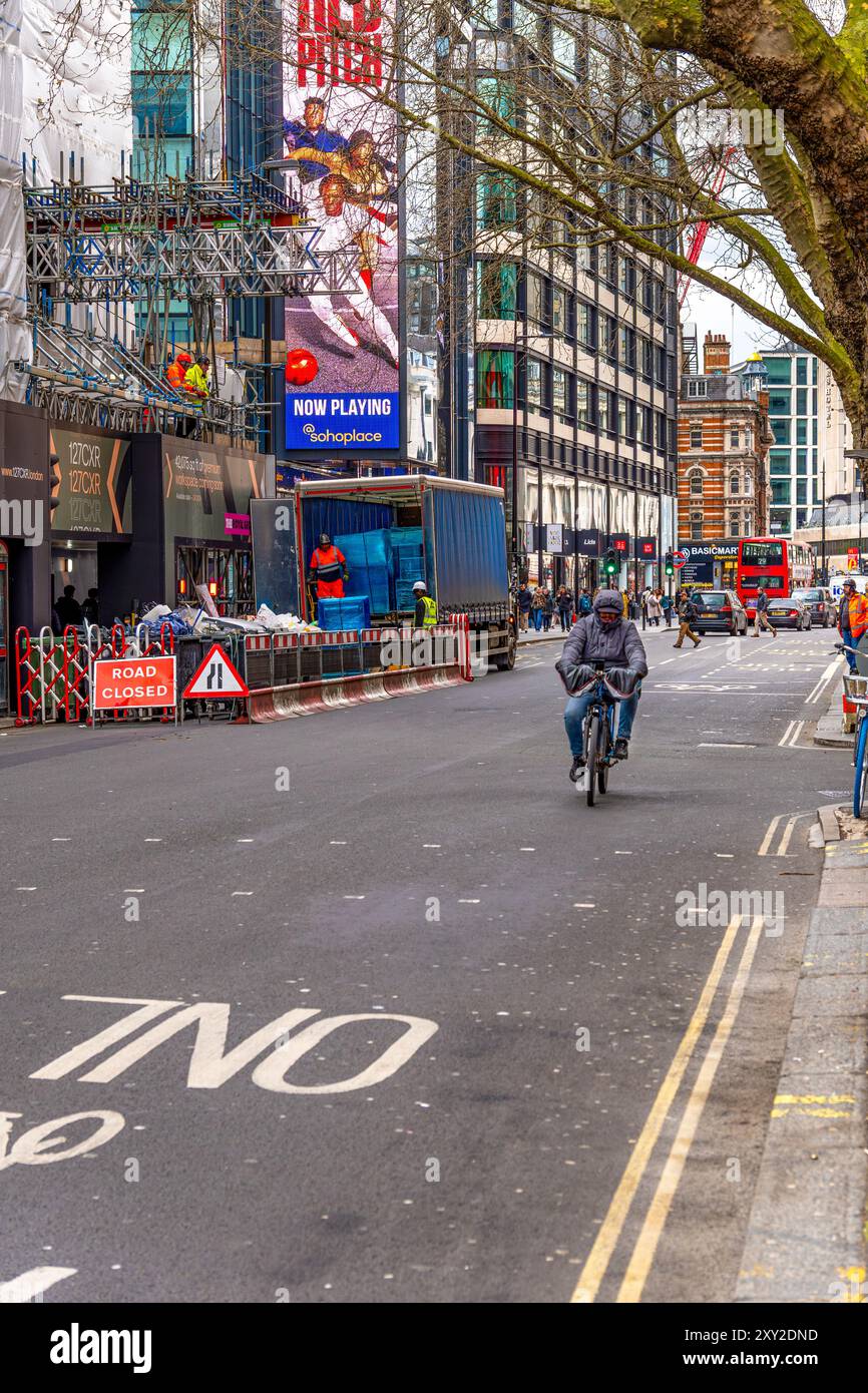 Rue du centre de Londres avec un bâtiment en construction avec échafaudage et ouvriers déchargeant des matériaux de construction d'un camion et d'un cycliste passi Banque D'Images