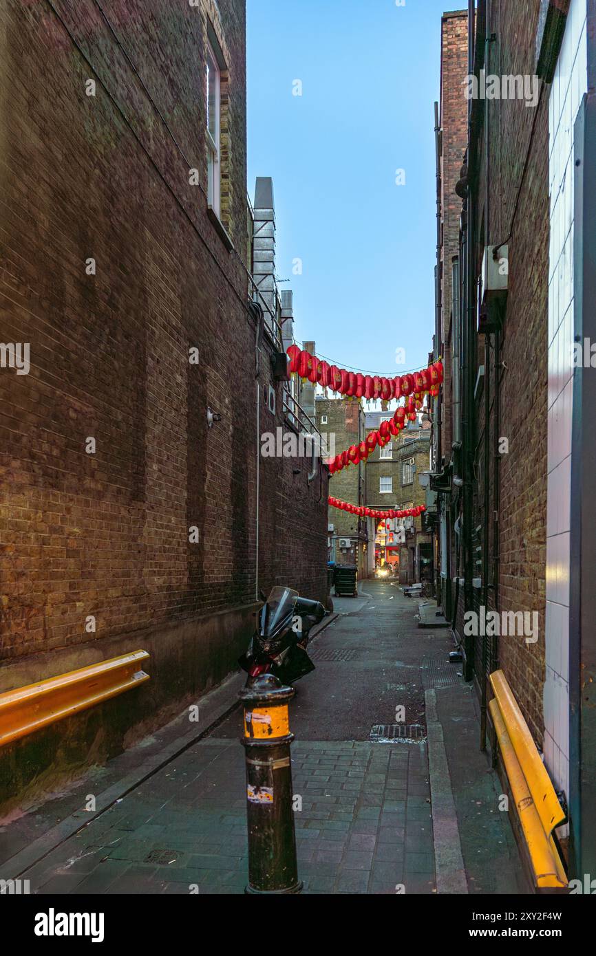 Ruelle sombre et étroite dans Chinatown avec des conteneurs de restaurant et des lanternes chinoises rouges suspendues entre les murs et une moto garée et une autre ap Banque D'Images