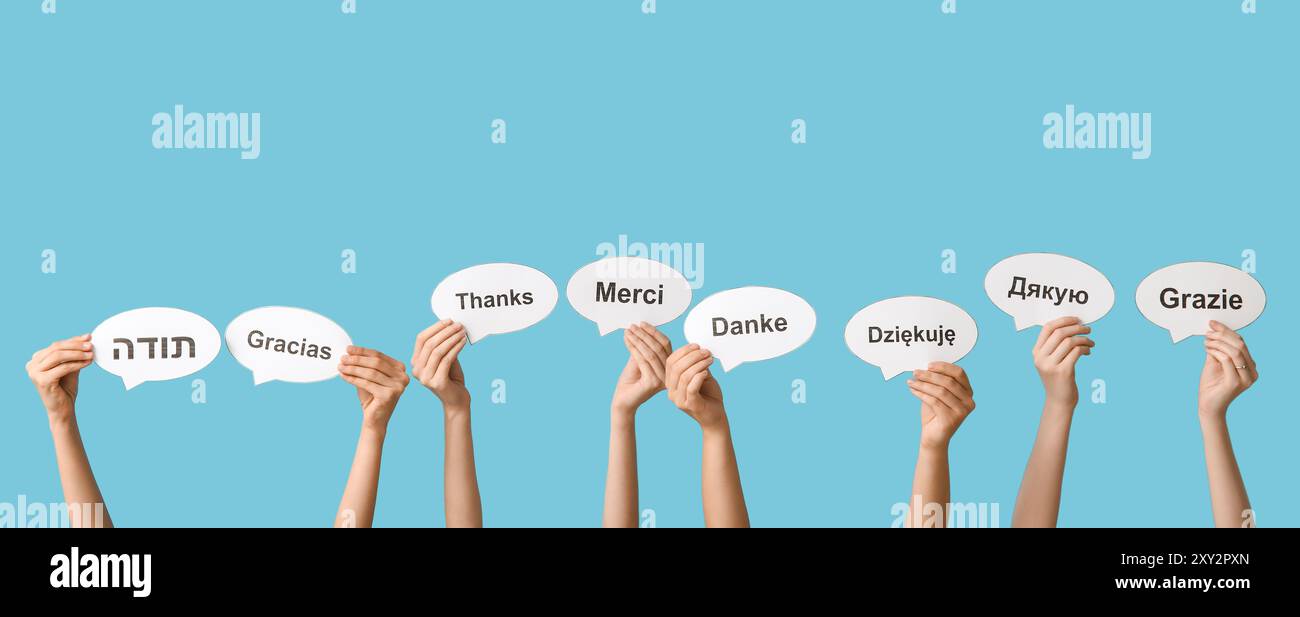 Mains tenant des bulles de parole avec du texte MERCI dans différentes langues sur fond bleu Banque D'Images