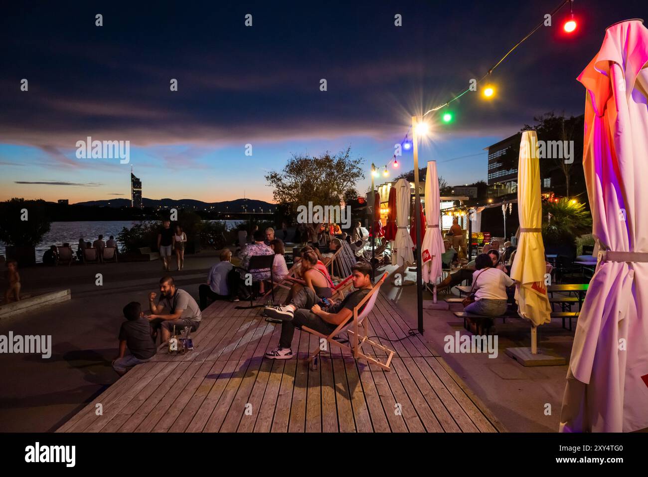 Jeunes assis sur la rive du Nouveau Danube au Bar D'arepa à Copa Beach au crépuscule, Vienne, Autriche Banque D'Images