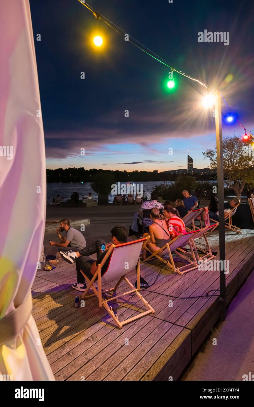 Jeunes assis sur la rive du Nouveau Danube au Bar D'arepa à Copa Beach au crépuscule, Vienne, Autriche Banque D'Images