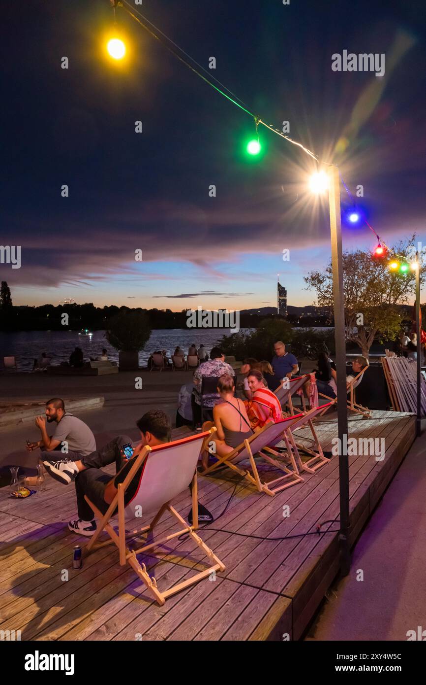 Jeunes assis sur la rive du Nouveau Danube au Bar D'arepa à Copa Beach au crépuscule, Vienne, Autriche Banque D'Images