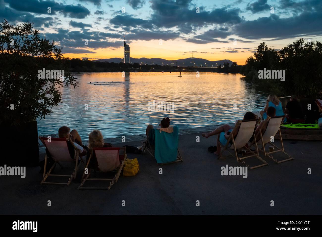 Personnes assises sur la rive du Nouveau Danube à Copa Beach pendant le coucher du soleil, Vienne, Autriche Banque D'Images