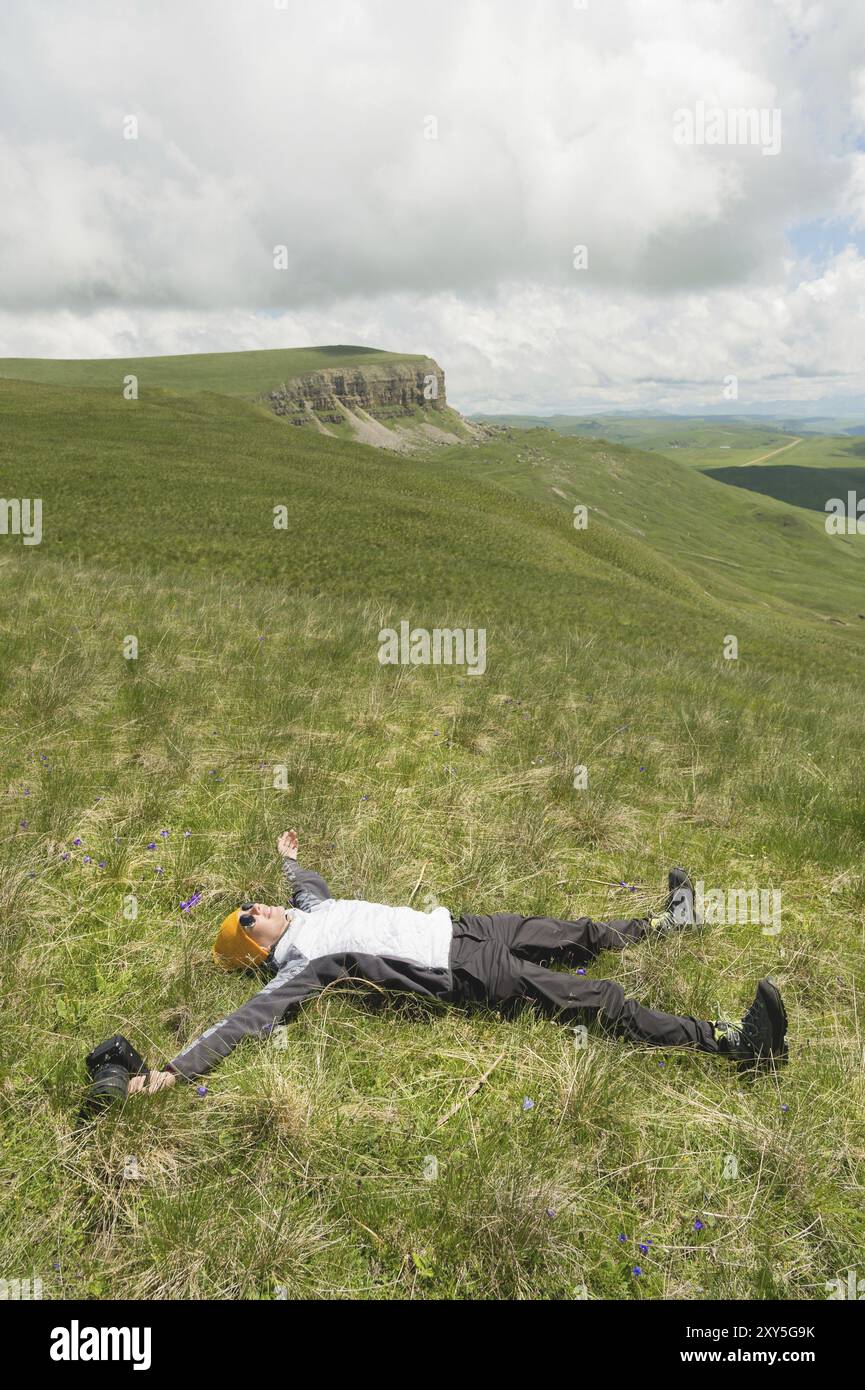 Photographe de fille heureuse dans des lunettes de soleil et avec un appareil photo à la main se trouve sur l'herbe écartant les bras et les jambes en dehors du bonheur de la liberté sur natur Banque D'Images