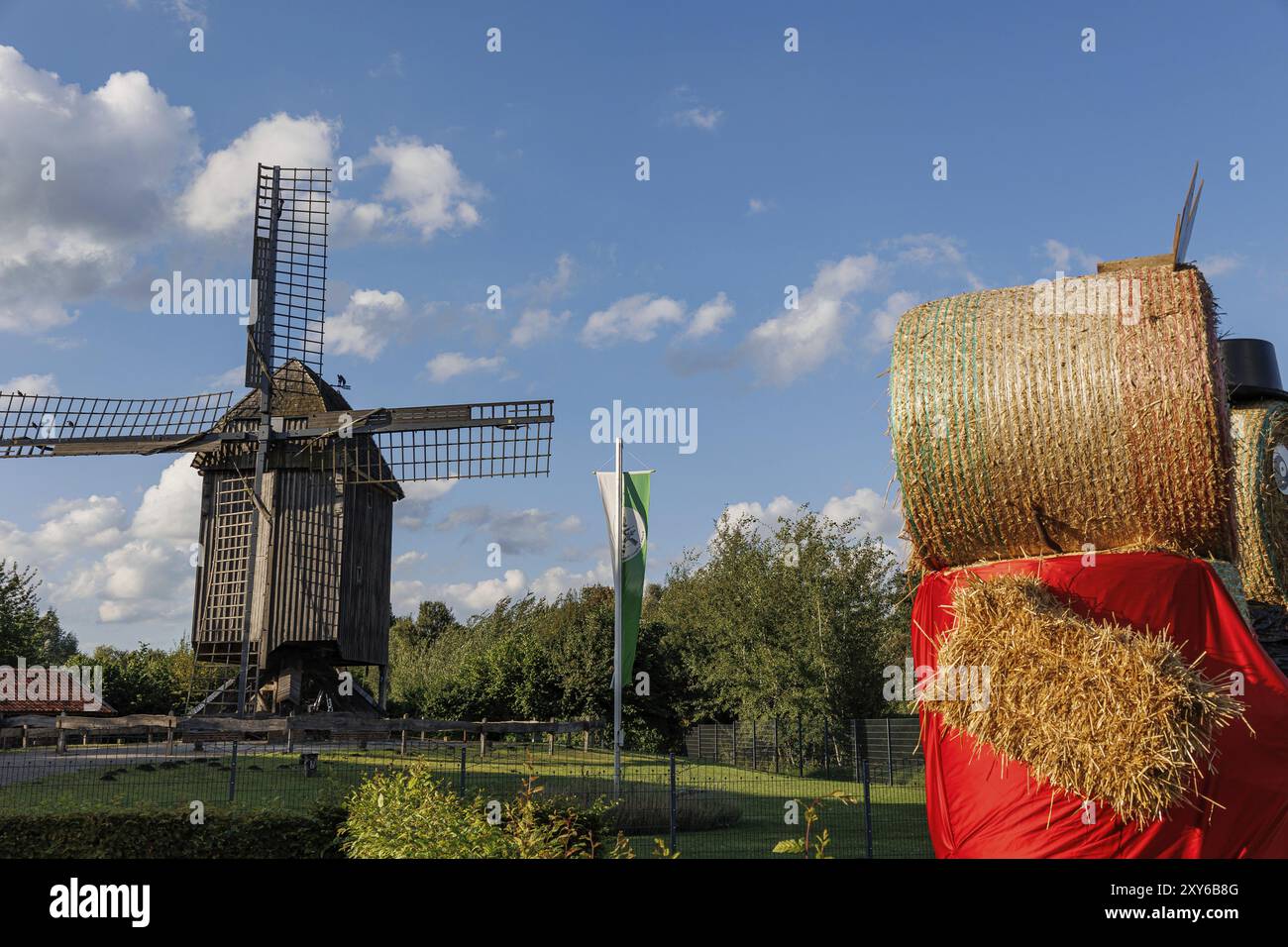 Un grand homme de paille en rouge se tient devant un moulin à vent et un drapeau vert et blanc sous un ciel bleu, weseke, muensterland, allemagne Banque D'Images