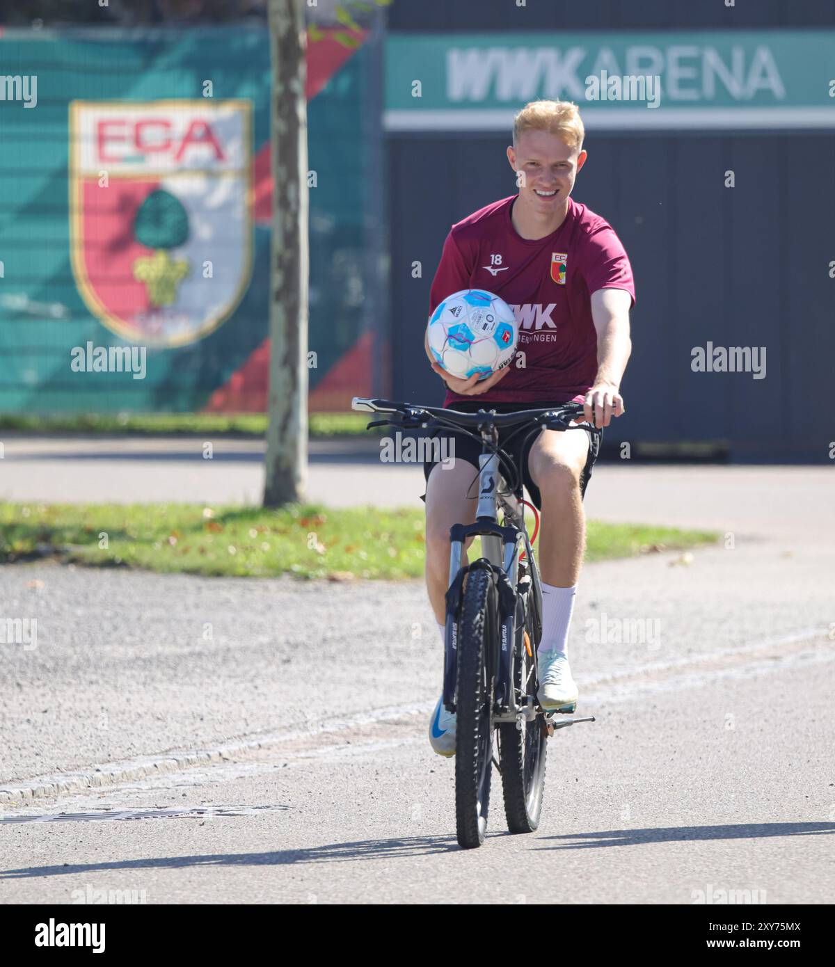 Tim Breithaupt (FC Augsburg #18) mit dem Fahrrad auf dem Weg zum Trainingsplatz, einen Fußball in der Hand, im Hintergrund WWK-Arena und FCA-logo ; FC Augsburg, entraînement, Banque D'Images