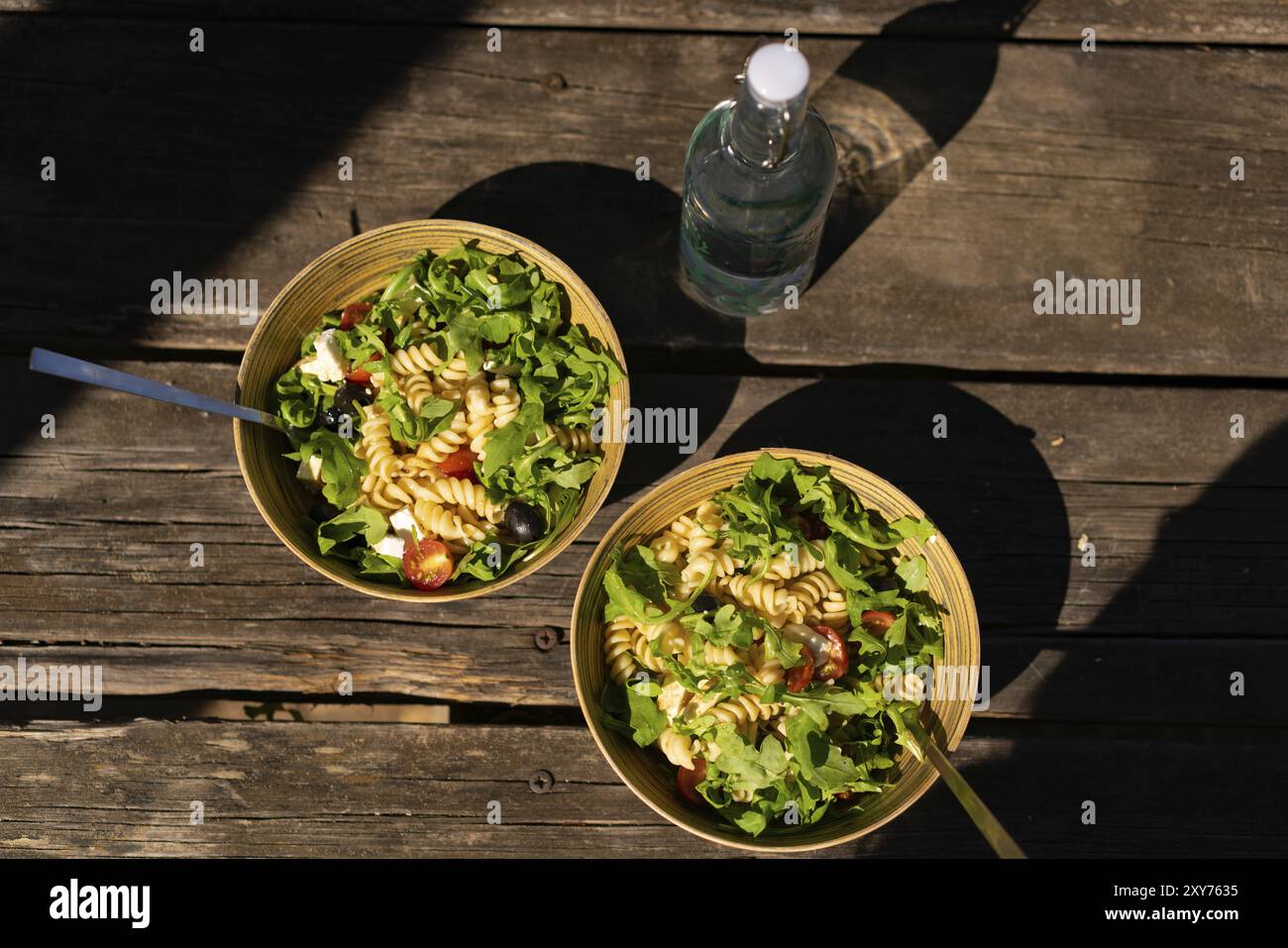 Salade méditerranéenne grecque avec fromage feta, pâtes, olives, tomates cerises et roquette sur un bol en bambou sur une table de pique-nique en bois à l'extérieur Banque D'Images