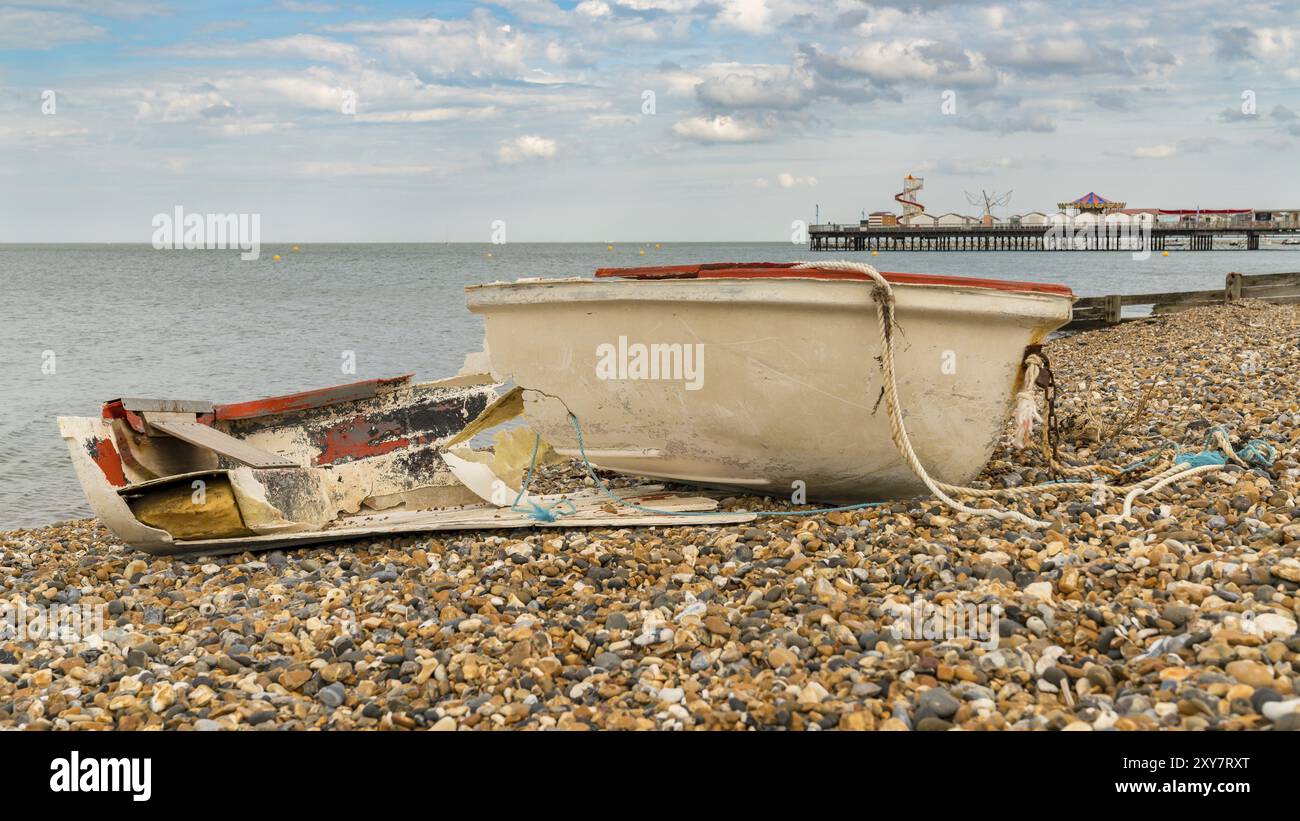 Un bateau cassé sur la plage de galets de Herne Bay, Kent, Angleterre, Royaume-Uni, avec Herne Pier en arrière-plan Banque D'Images