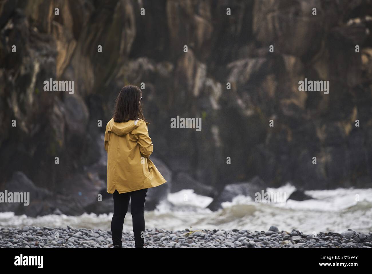 Sur une Femme Veste pluie jaune à la recherche de la mer avec des pierres sur l'arrière-plan, à Madère Banque D'Images