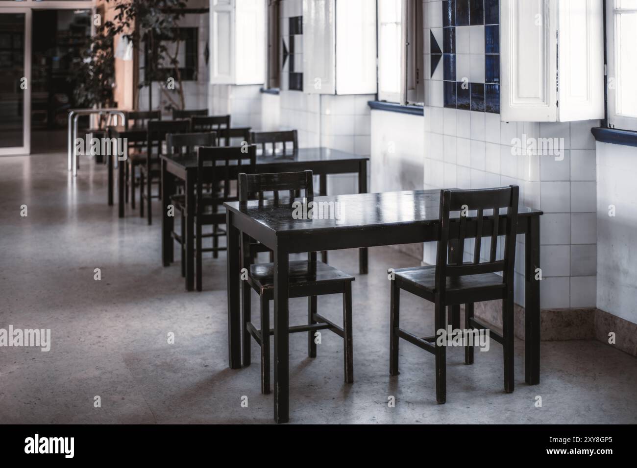 Intérieur vide d'un café minimaliste avec des tables et des chaises en bois noir disposées en rangées contre un mur carrelé avec des motifs bleus et blancs. L'espace Banque D'Images
