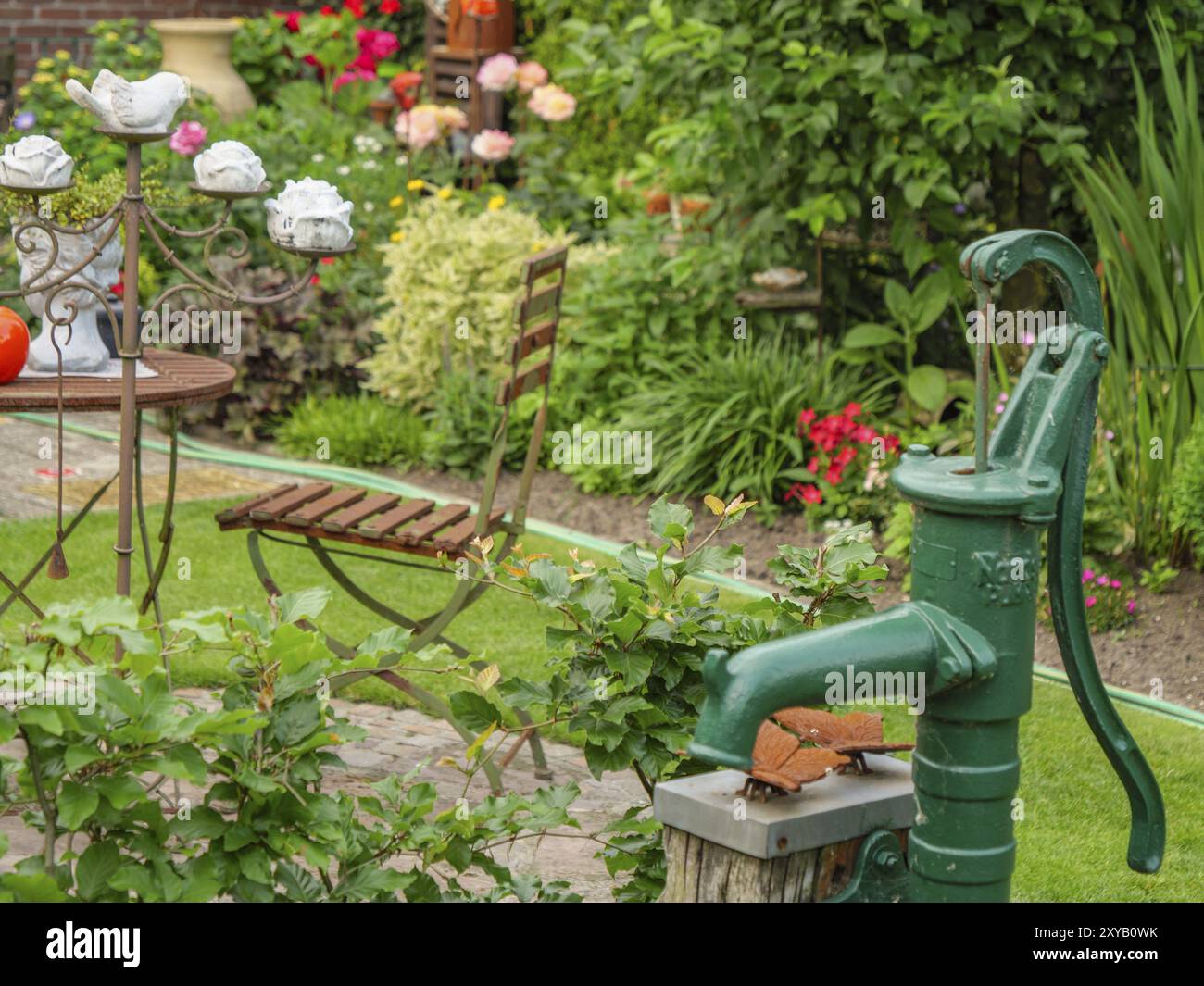 Jardin vert avec une pompe à eau antique à côté d'une table et des chaises et diverses plantes, borken, muensterland, allemagne Banque D'Images