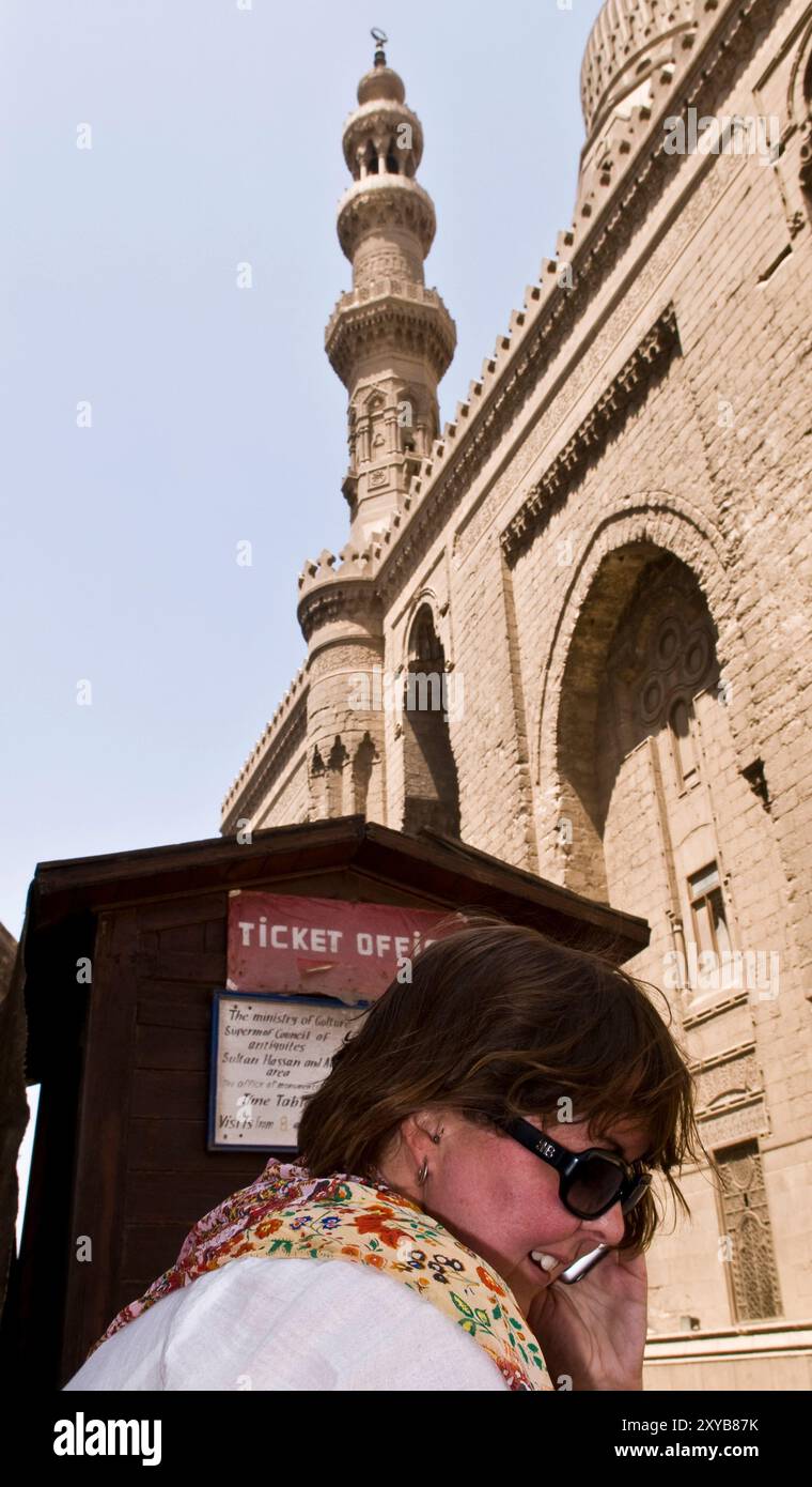 Une touriste parle sur son téléphone portable devant la porte de Madrassa du sultan Hassan & Al Rifa'i mosquée près de la citadelle au Caire, en Egypte. Banque D'Images