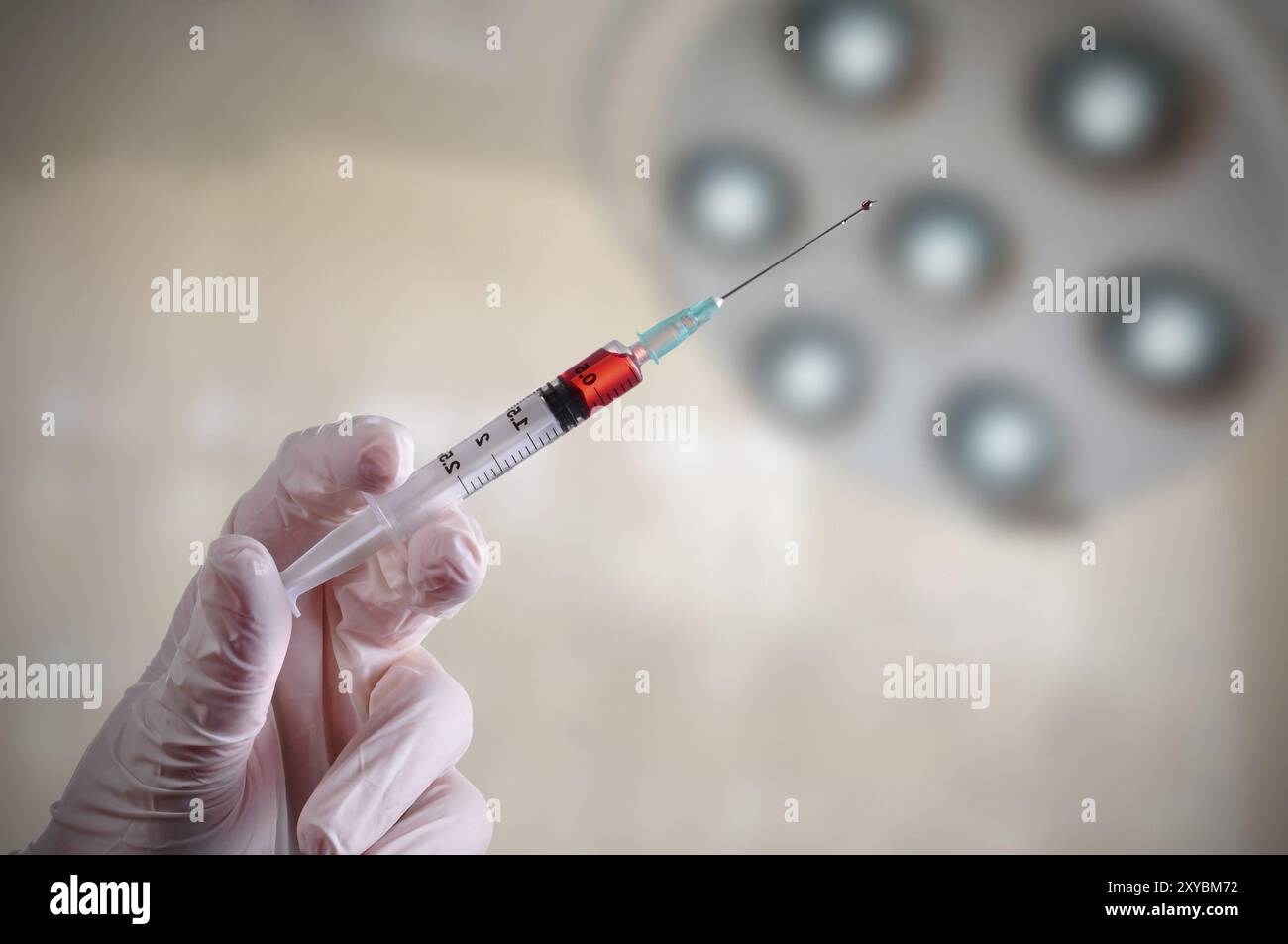 Gants en latex avec la main tenant une seringue d'un liquide rouge à l'intérieur, dans une salle d'opération Banque D'Images