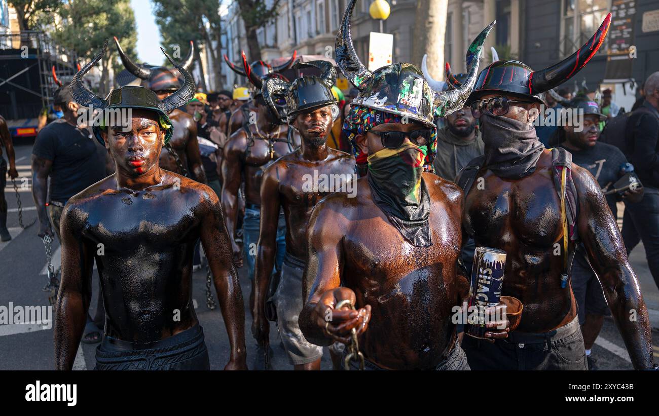 Le jab jab remonte aux plantations de Grenade à l'époque de l'esclavage. L'huile, la graisse et la peinture noire remplacent la mélasse qui a été utilisée pour couvrir leur corps. Des chaînes épaisses et lourdes sont traînées dans les rues, des cornes de chèvre portées sur la tête avec des langues rouges ou de la chair crue collant à l'extérieur de leur bouche. D'autres accessoires utilisés comprennent les poussettes de bébé avec des tambours d'huile de poupées, des boîtes à biscuits et des coquilles de conque sont leurs instruments car ils sont battus hypnotiquement comme le jab jab défilent dans les rues. Siroter du rhum, le produit de la mélasse et de leur sang et larmes Banque D'Images