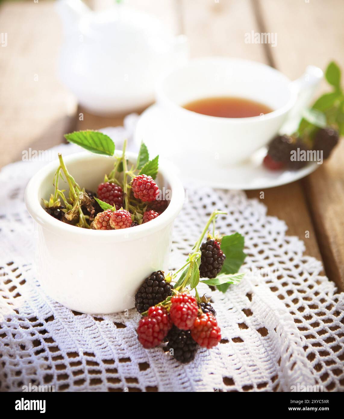 De dessus de framboise fraîche et de mûre avec des feuilles vertes sur table en bois avec un tissu tricoté blanc et une tasse de thé aromatique Banque D'Images