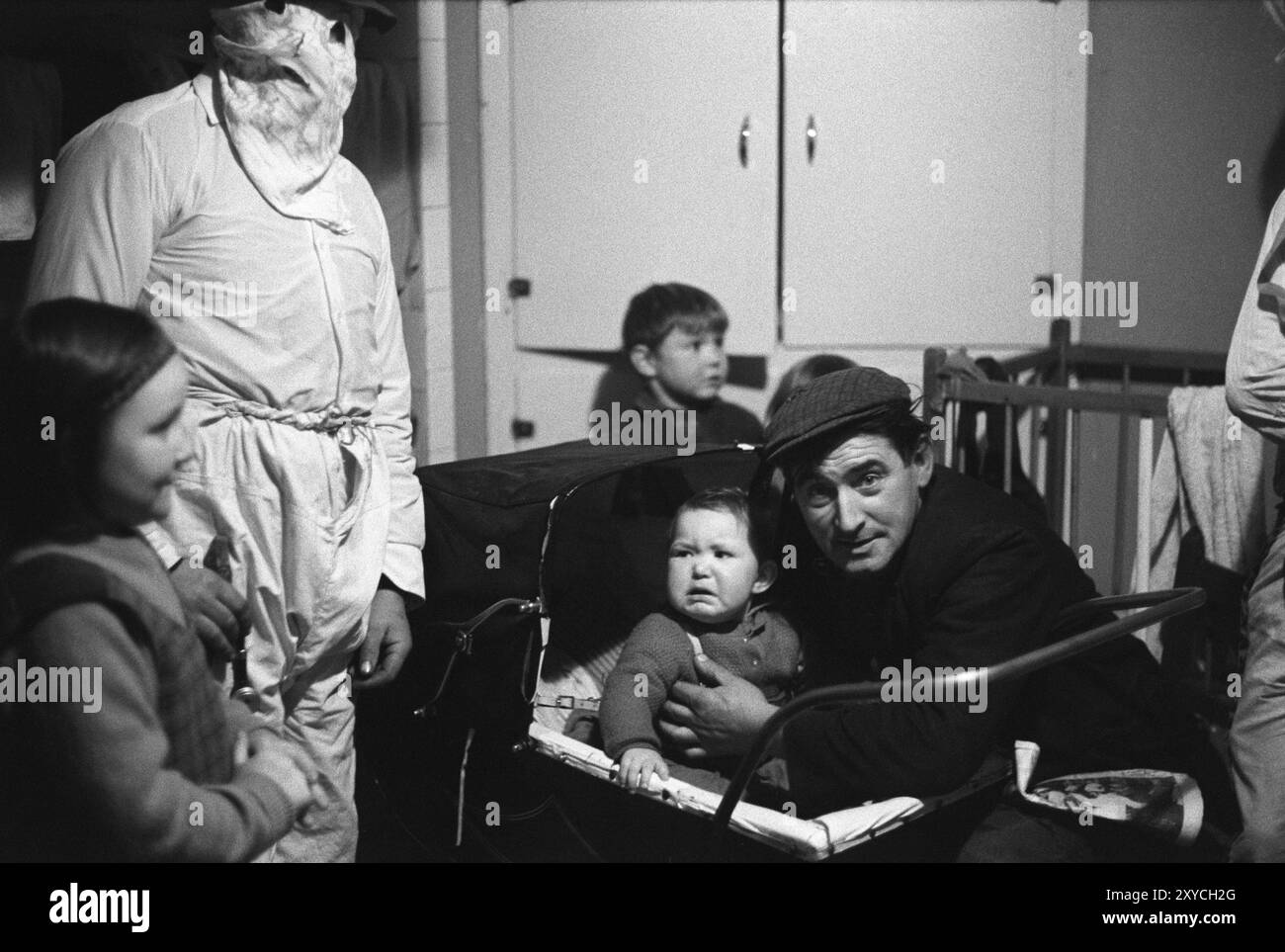 Effrayé, pleurant bébé effrayé dans la poussette avec le père. Les Biddy Boys font une visite à la maison et le chid est terrifié par les masques que les Biddy Boys portent. Killorglin, County Kerry, Eire, Irlande du Sud février 1972 1970s HOMER SYKES Banque D'Images