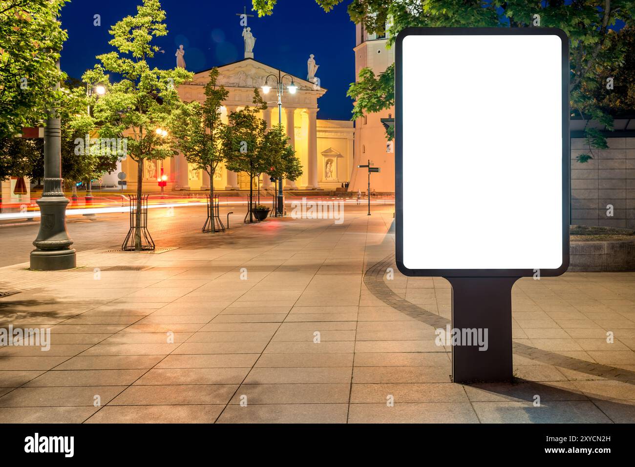 Maquette de panneau d'affichage sur le trottoir la nuit. Écran publicitaire vide devant l'église Banque D'Images