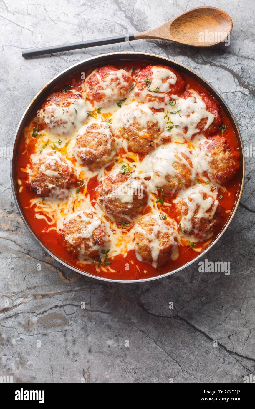Boulettes de viande cuites dans une sauce tomate avec du fromage mozzarella et du thym gros plan dans un plat allant au four sur la table. Vue de dessus verticale Banque D'Images