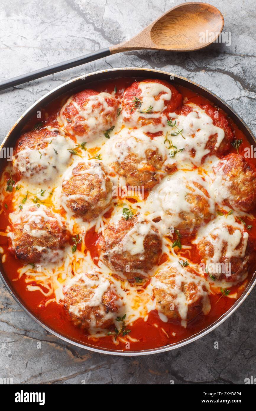 Gros plan d'une casserole de boulettes de viande dans une sauce tomate avec du fromage mozzarella dans un plat allant au four sur la table. Vue de dessus verticale Banque D'Images