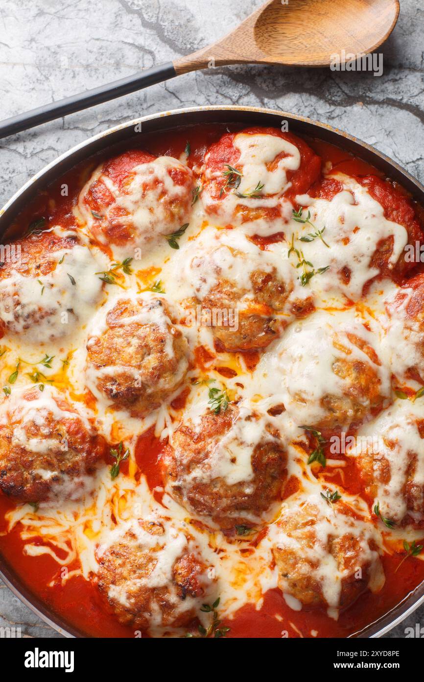 Casserole de boulettes de viande maison dans une sauce tomate épicée avec fromage mozzarella et thym gros plan dans un plat allant au four sur la table. Vue de dessus verticale de ci-dessus Banque D'Images
