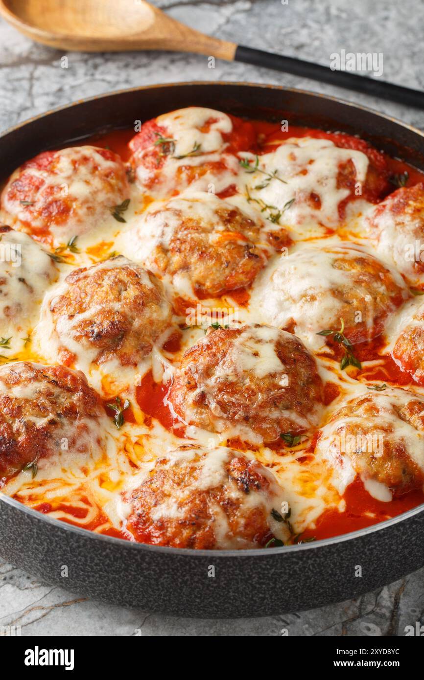 Gros plan d'une casserole de boulettes de viande dans une sauce tomate avec du fromage mozzarella dans un plat allant au four sur la table. Vertical Banque D'Images