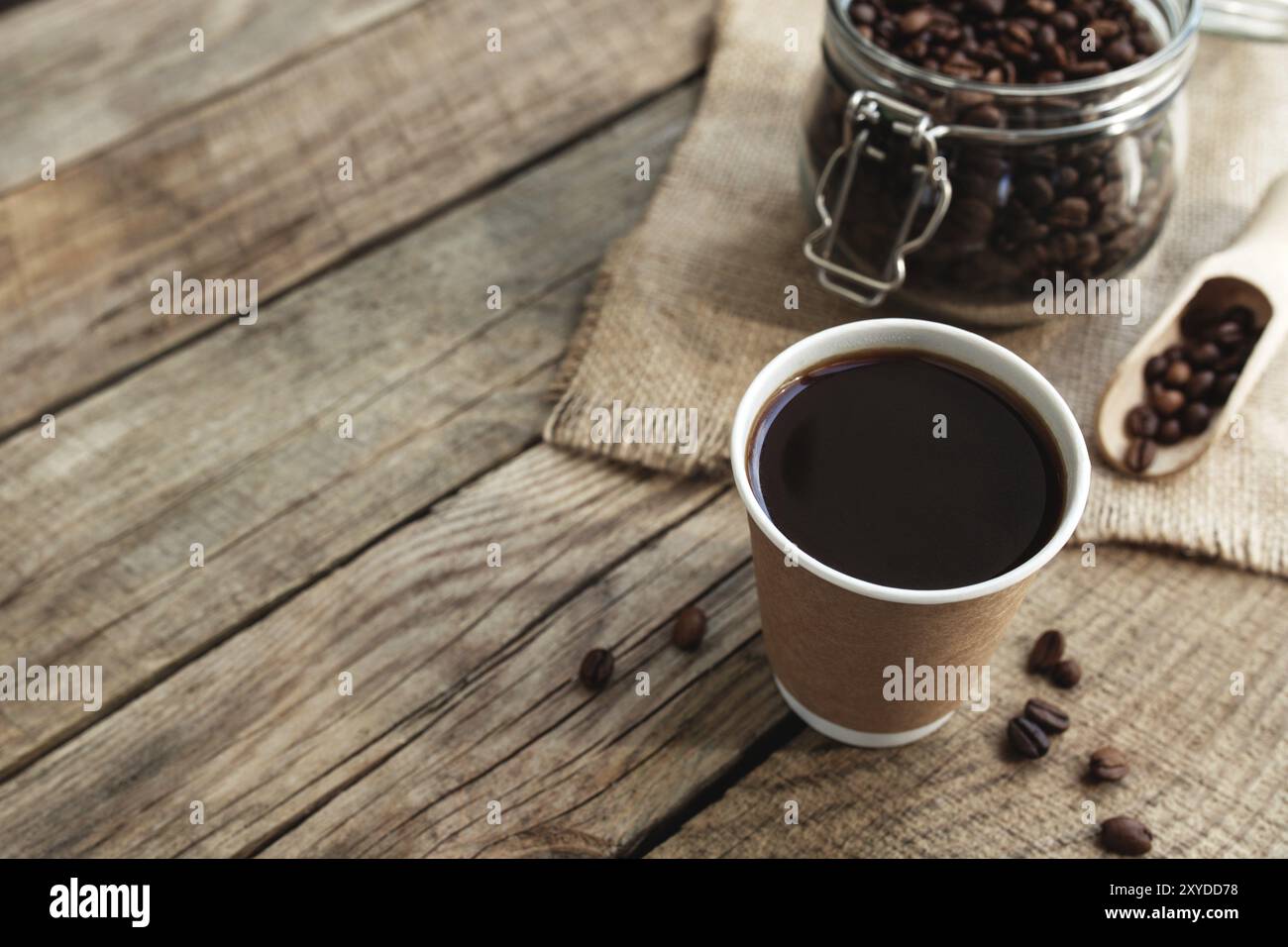 Concept de petit déjeuner au café avec une tasse de papier de café noir expresso, café torréfié sec grains dans le pot en verre et cuillère à l'ancienne table en bois Banque D'Images