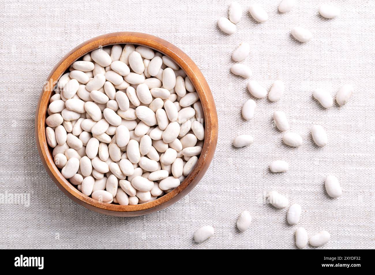Haricots blancs dans un bol en bois sur tissu de lin. Petites graines séchées, une variété de Phaseolus vulgaris, le haricot commun, un membre de la famille des légumineuses. Banque D'Images