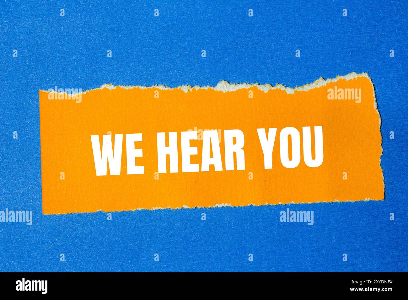 Nous entendons vous message écrit sur papier orange déchiré déchiré avec fond bleu. Conceptuel nous entendons vous symbole. Copier l'espace. Banque D'Images