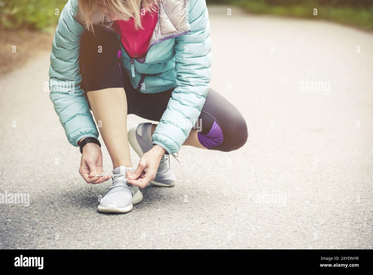 Portrait d'une jeune fille blonde sportive dans des écouteurs sur une course dans la forêt. Une fille assise à lacets noués sur des chaussures de cross-country. Mode de vie actif. Sport Banque D'Images