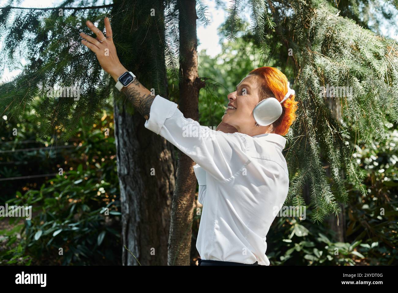 Une enseignante sourit en touchant une branche d'arbre et en écoutant de la musique. Banque D'Images