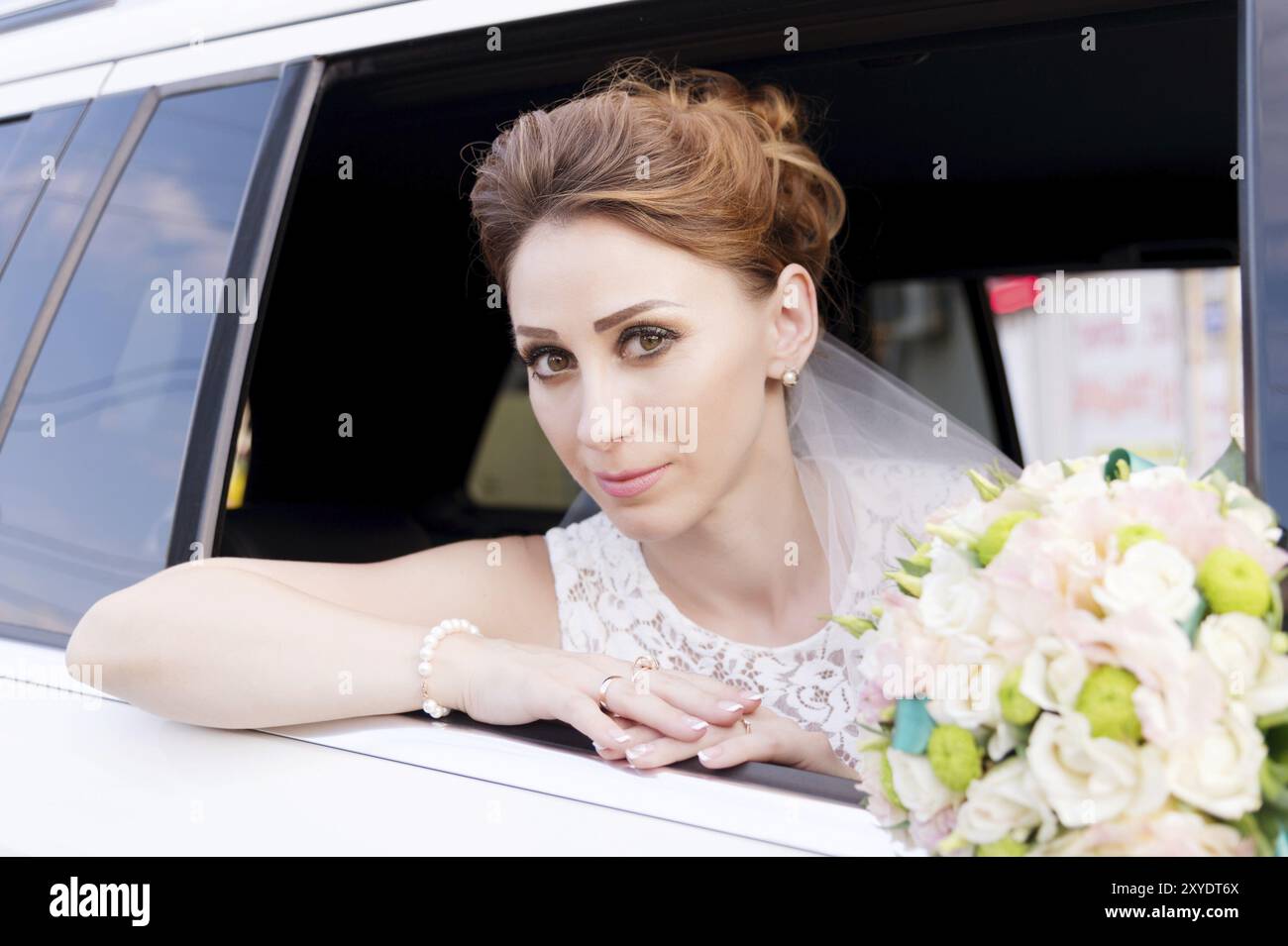 Gros plan portrait d'une belle mariée à côté de son bouquet de mariage dans la fenêtre d'une voiture de mariage. Le concept de grâce de mariage Banque D'Images