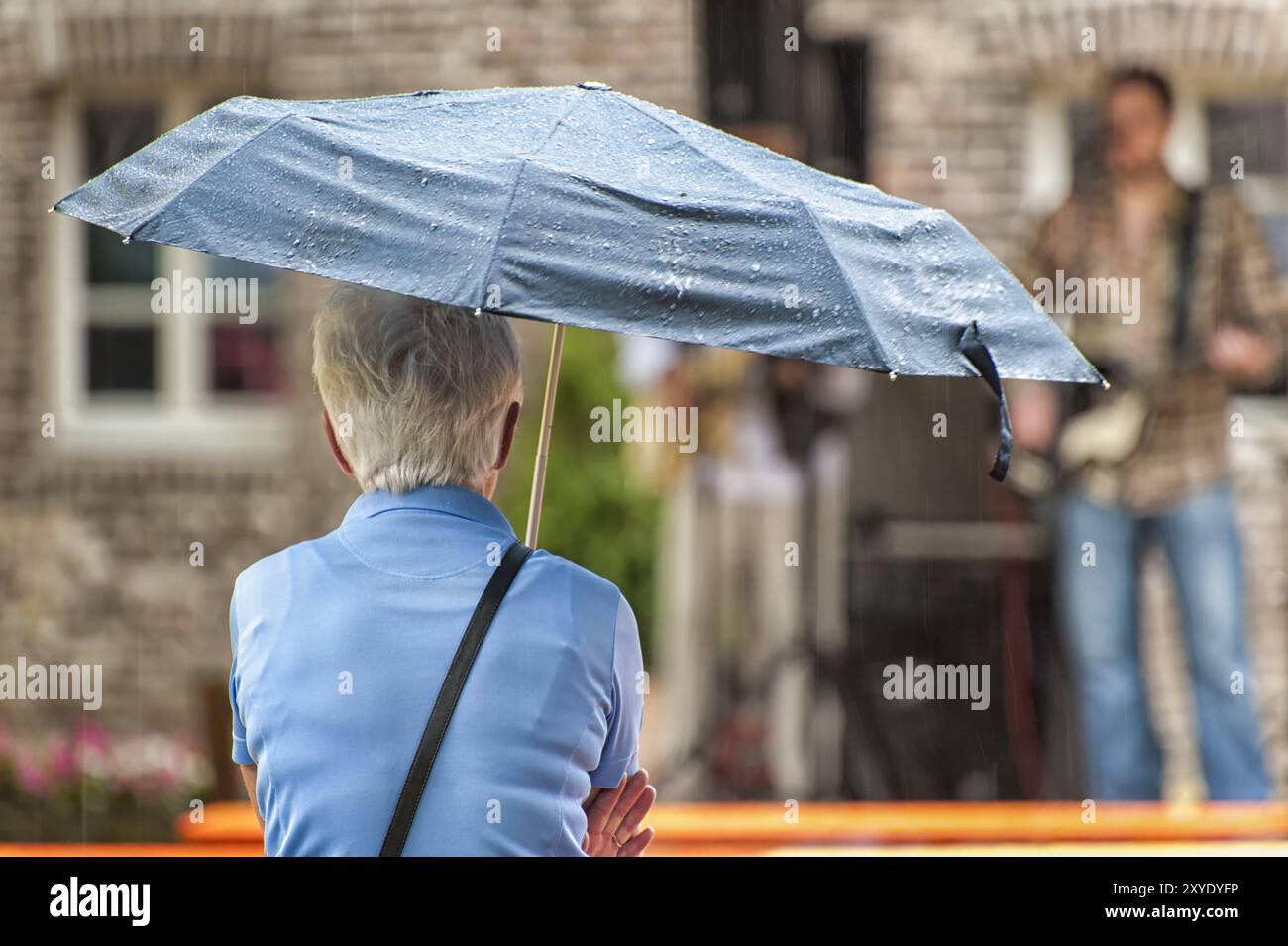 Une personne âgée est assise sous un parapluie Banque D'Images