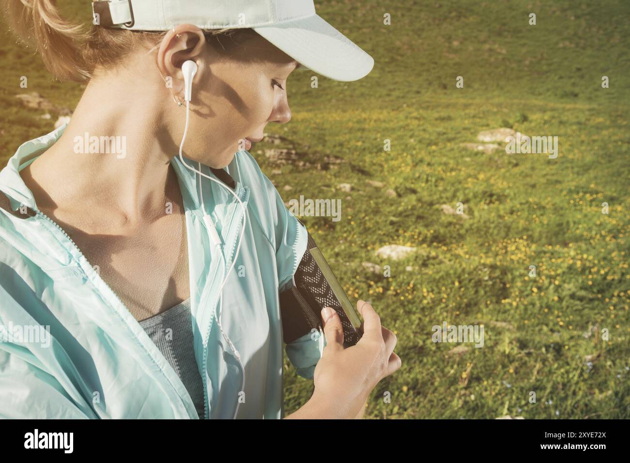 Gros plan Une femme sportive dans une casquette et nuzhniki bascule les chansons sur son téléphone portable lors d'un exercice en plein air sur fond de champs et R Banque D'Images Gros plan Une femme sportive dans une casquette et nuzhniki bascule les chansons sur son téléphone portable lors d'un exercice en plein air sur fond de champs et R Banque D'Images