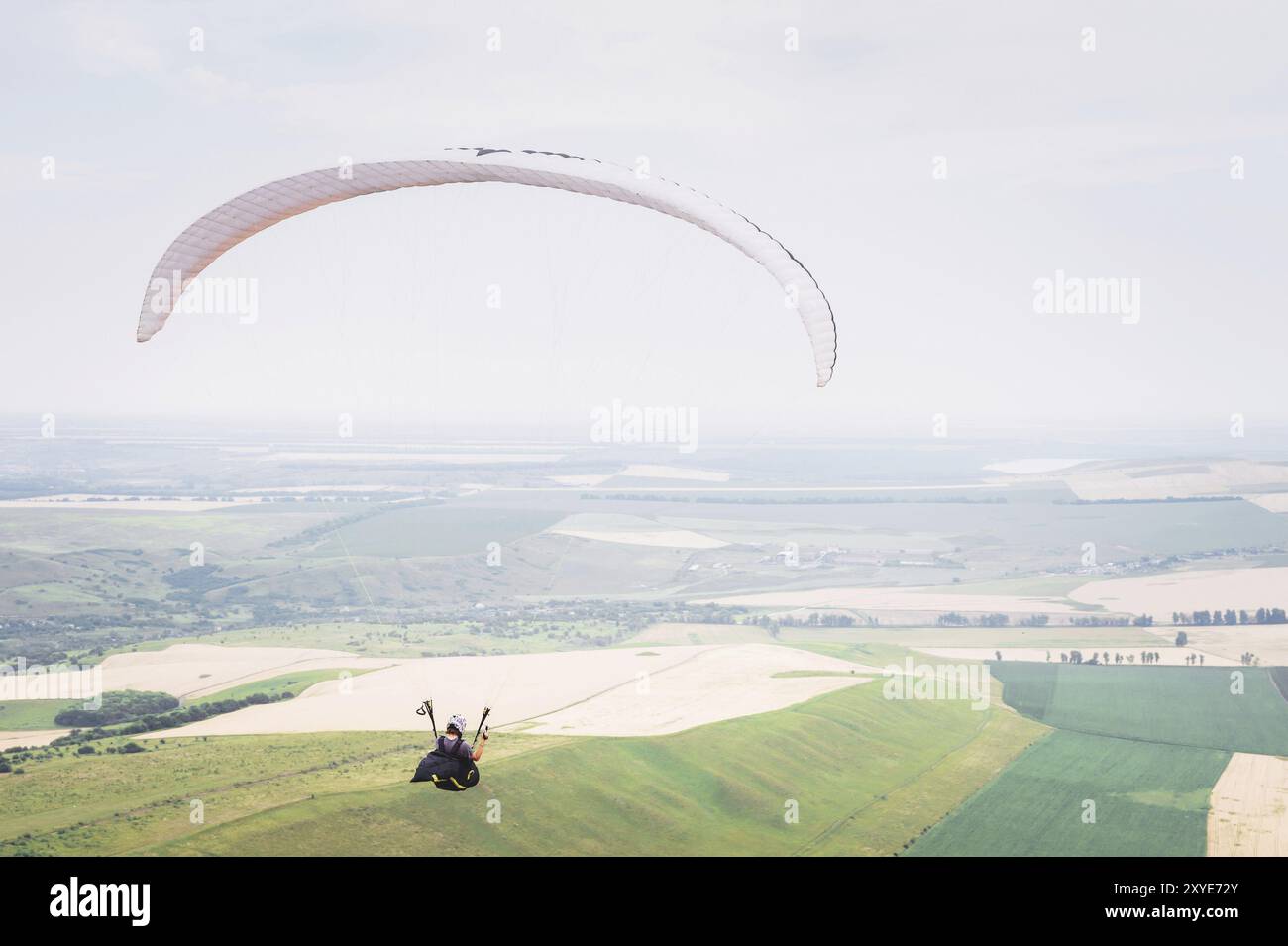 Parapente d'orange blanche avec parapente dans un cocon sur fond de champs du ciel et de nuages. Parapente Sports Banque D'Images