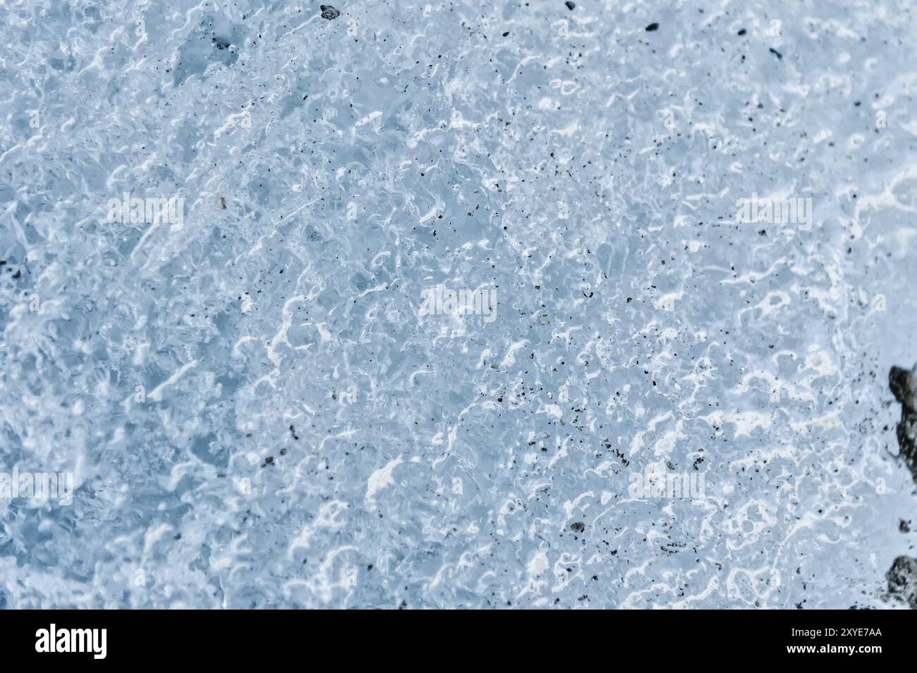 Gros plan de la surface d'un fragment d'un glacier avec une structure de bandes et de bulles entrecoupées de sable et de roches rocheuses. Texture bleu glacé à Banque D'Images