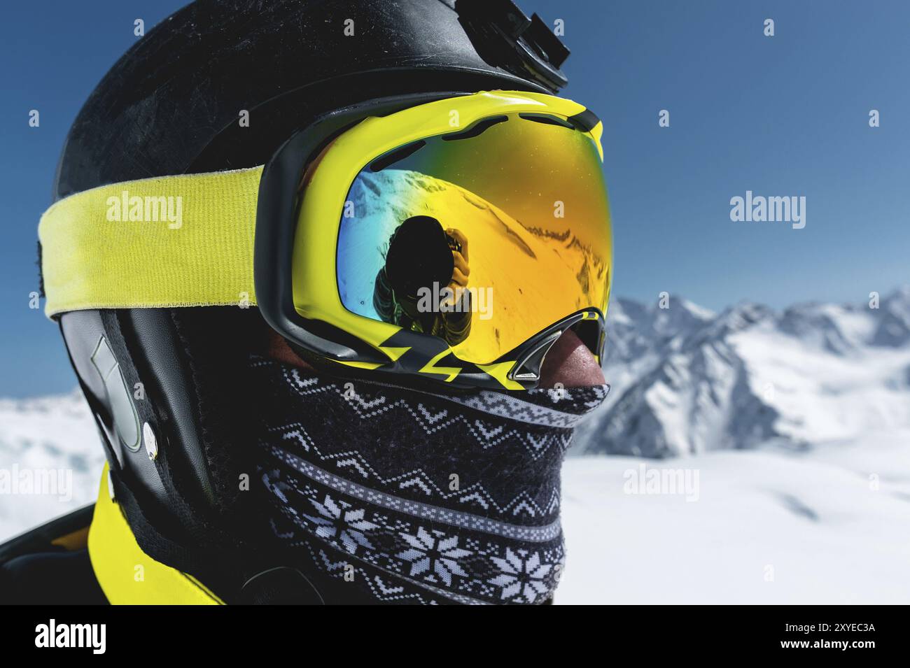 Gros plan d'un skieur dans un masque et un casque avec un visage fermé sur un fond de montagnes enneigées et de ciel bleu Banque D'Images