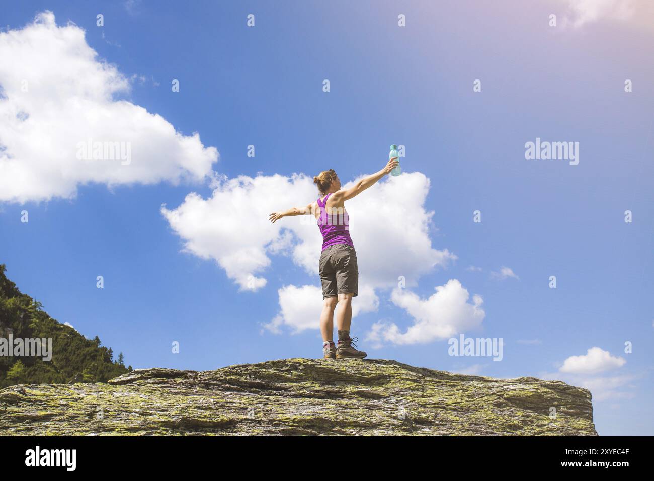 Objectif atteint : une jeune fille sportive est debout sur un gros rocher et lève les mains dans les airs Banque D'Images
