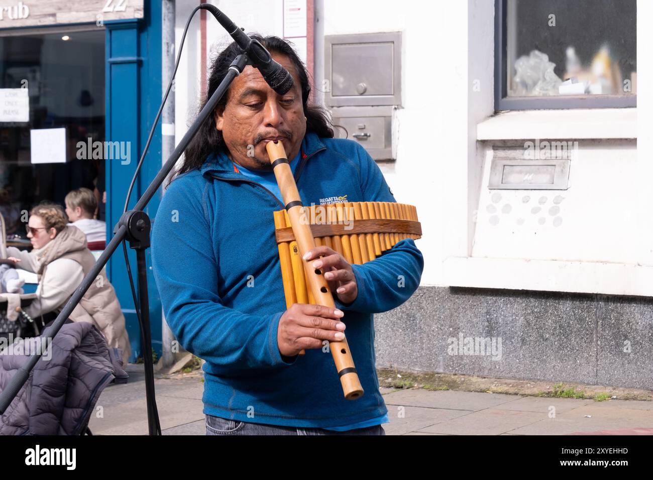 Homme aux longs cheveux noirs portant un haut bleu, jouant des instruments de musique traditionnels sud-américains à vent. Ballycastle, Royaume-Uni - 26 août 2024. Banque D'Images